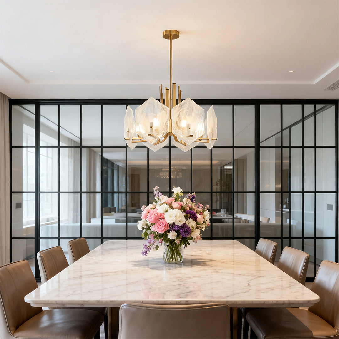 Bright transitional dining room where a gold geometric chandelier hangs above a white marble table separated by glass doors.