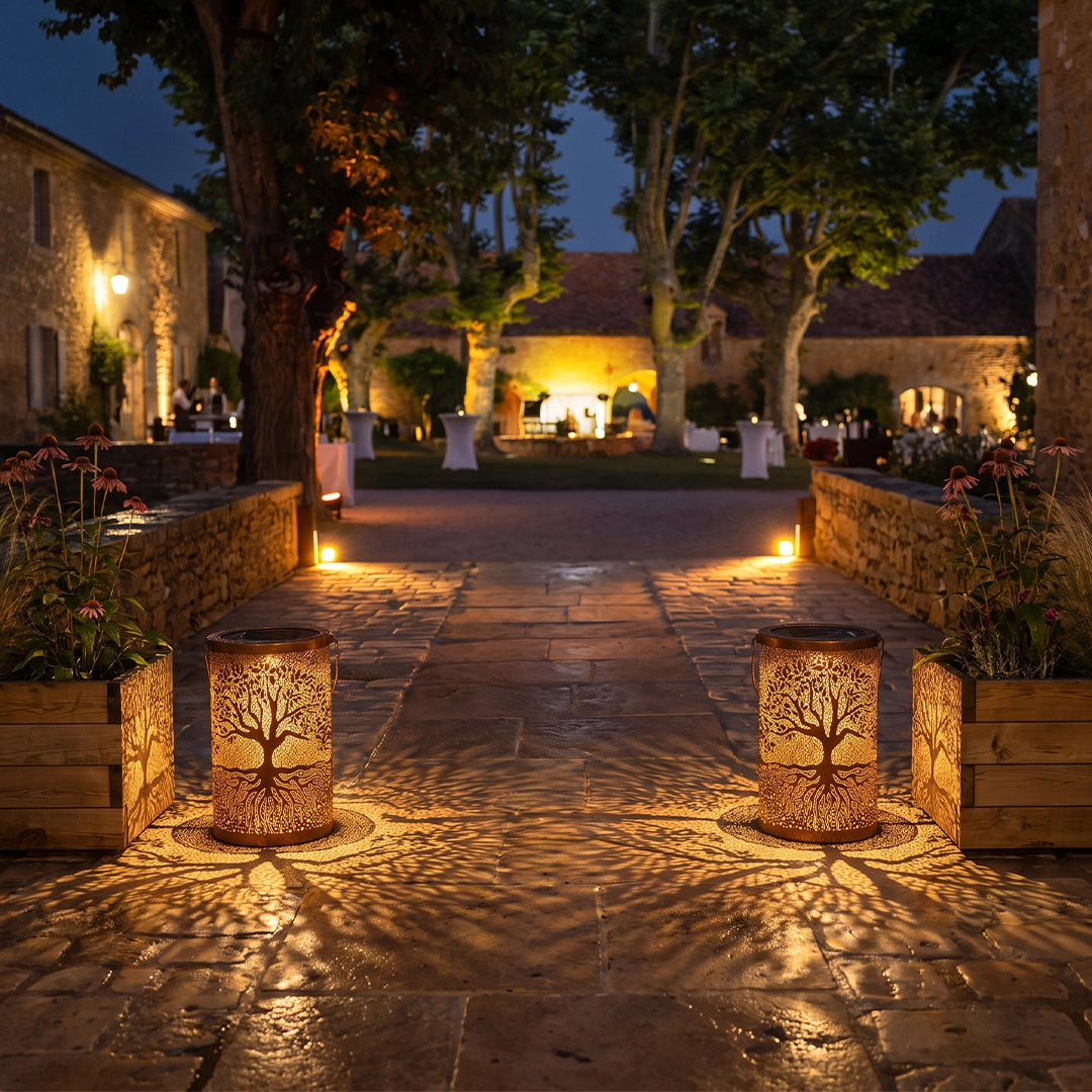 Tree of life lanterns illuminating a garden path and casting warm patterned light at night.