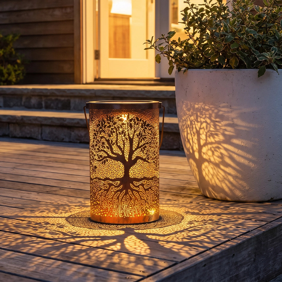Tree of life lantern glowing on a wooden patio and casting branch-shaped shadows beside a planter.