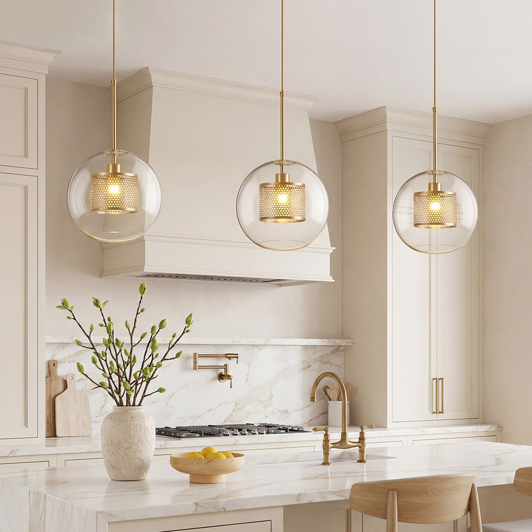 Trio of Clear Glass Globe Pendant lights with brass mesh interiors over a marble kitchen island.