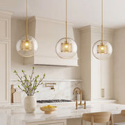 Trio of Clear Glass Globe Pendant lights with brass mesh interiors over a marble kitchen island.