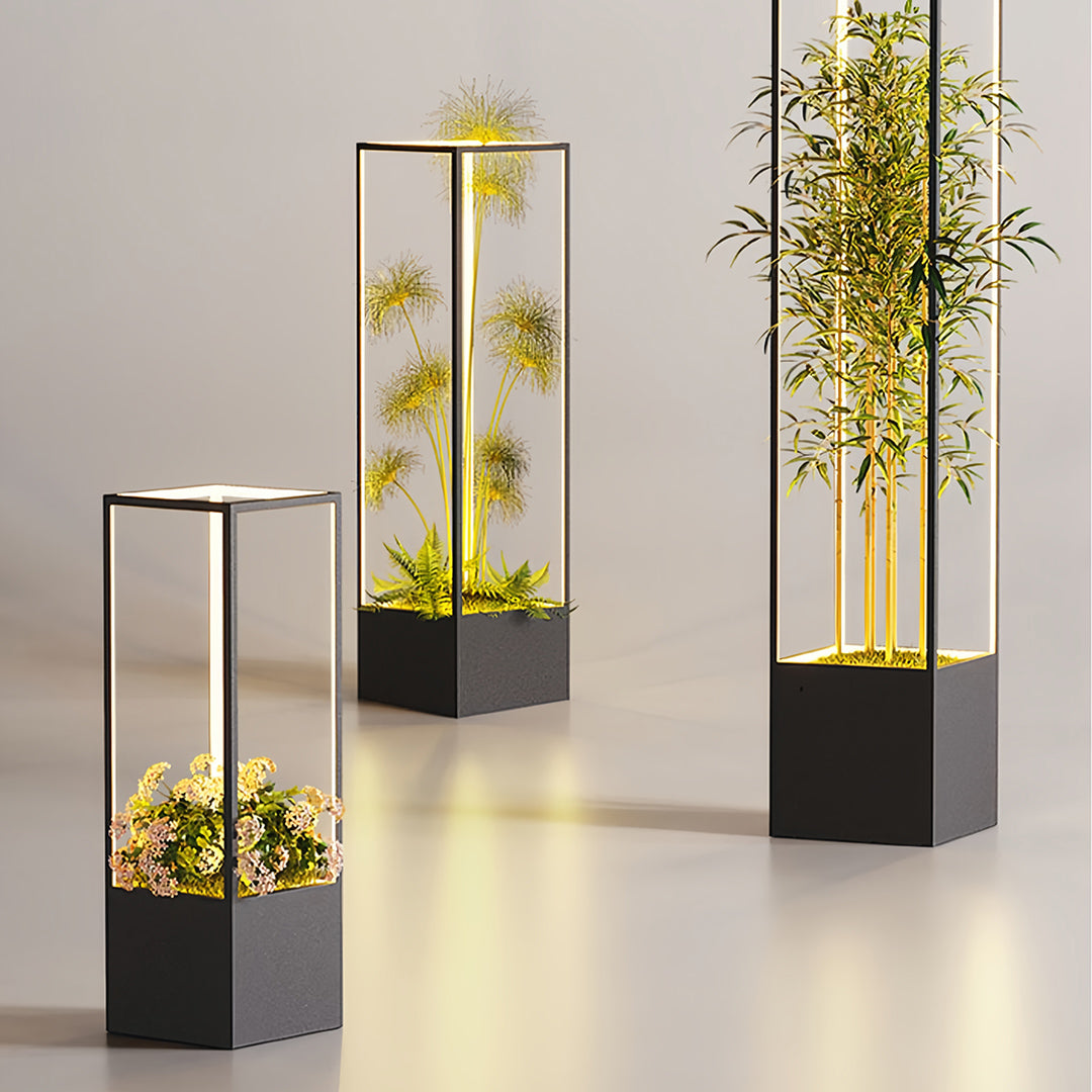 Trio of contemporary square floor lamps used as illuminated bollards in an outdoor setting, highlighting potted bamboo and foliage.