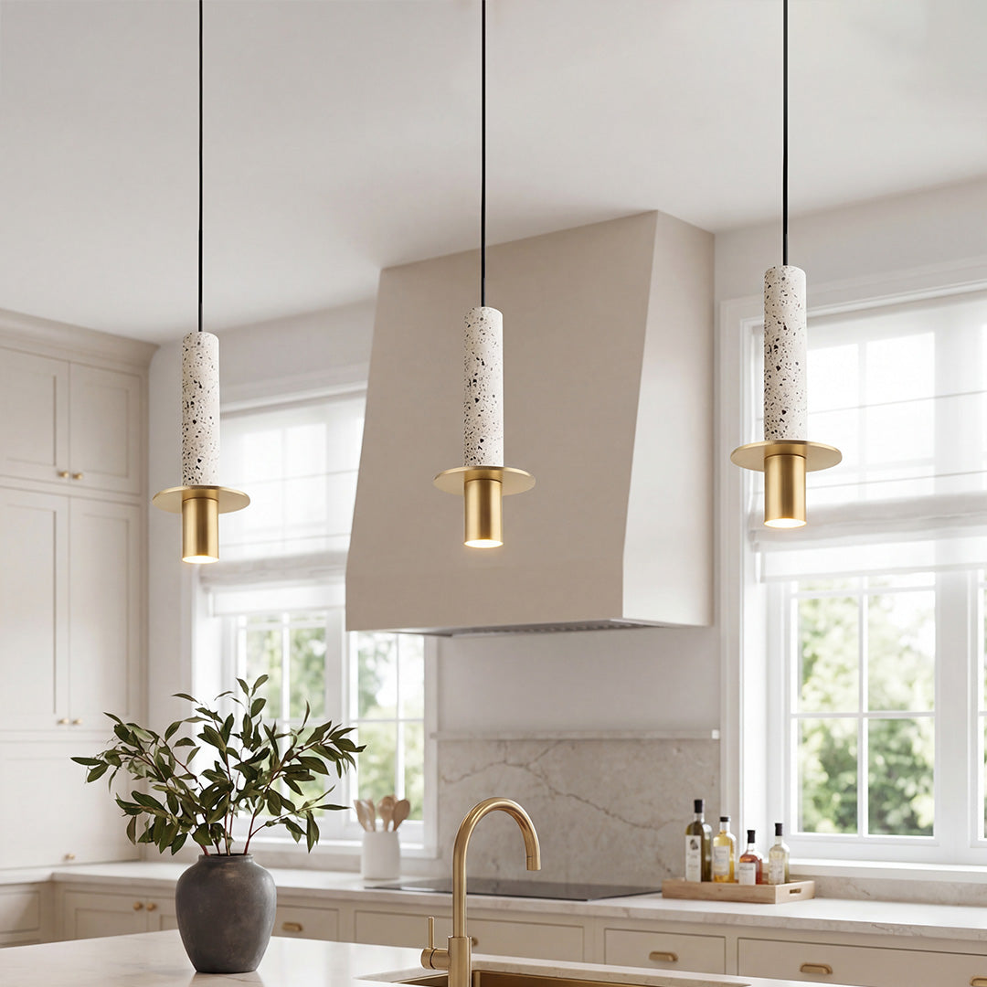 Trio of elegant white terrazzo cylinder pendant lights with gold hardware over a kitchen island.