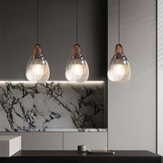 Triple hanging glass pendant lights arranged over kitchen island with marble backsplash