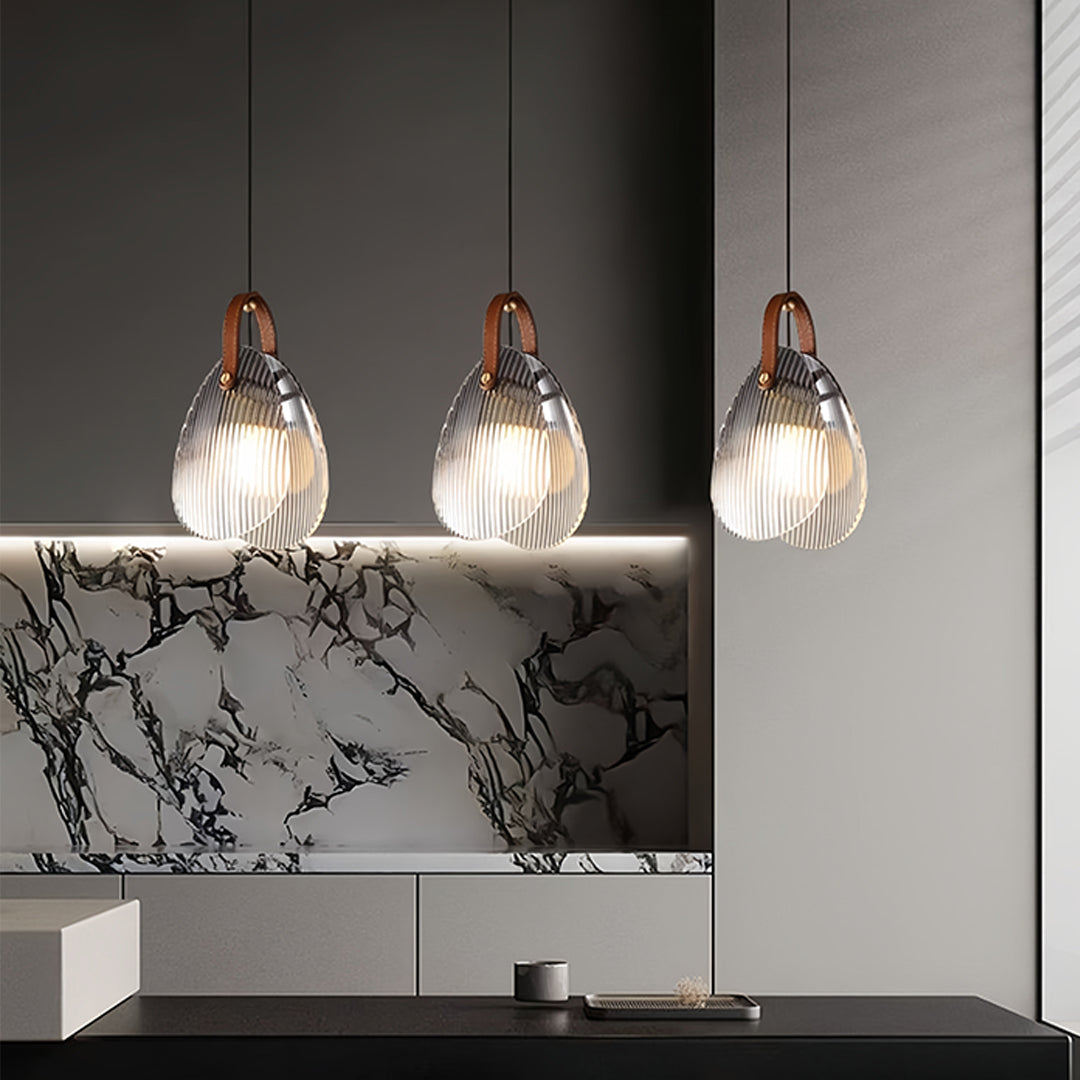 Triple hanging glass pendant lights arranged over kitchen island with marble backsplash