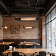 Tube pendant light installed above a wooden table in a modern industrial-style cafe.