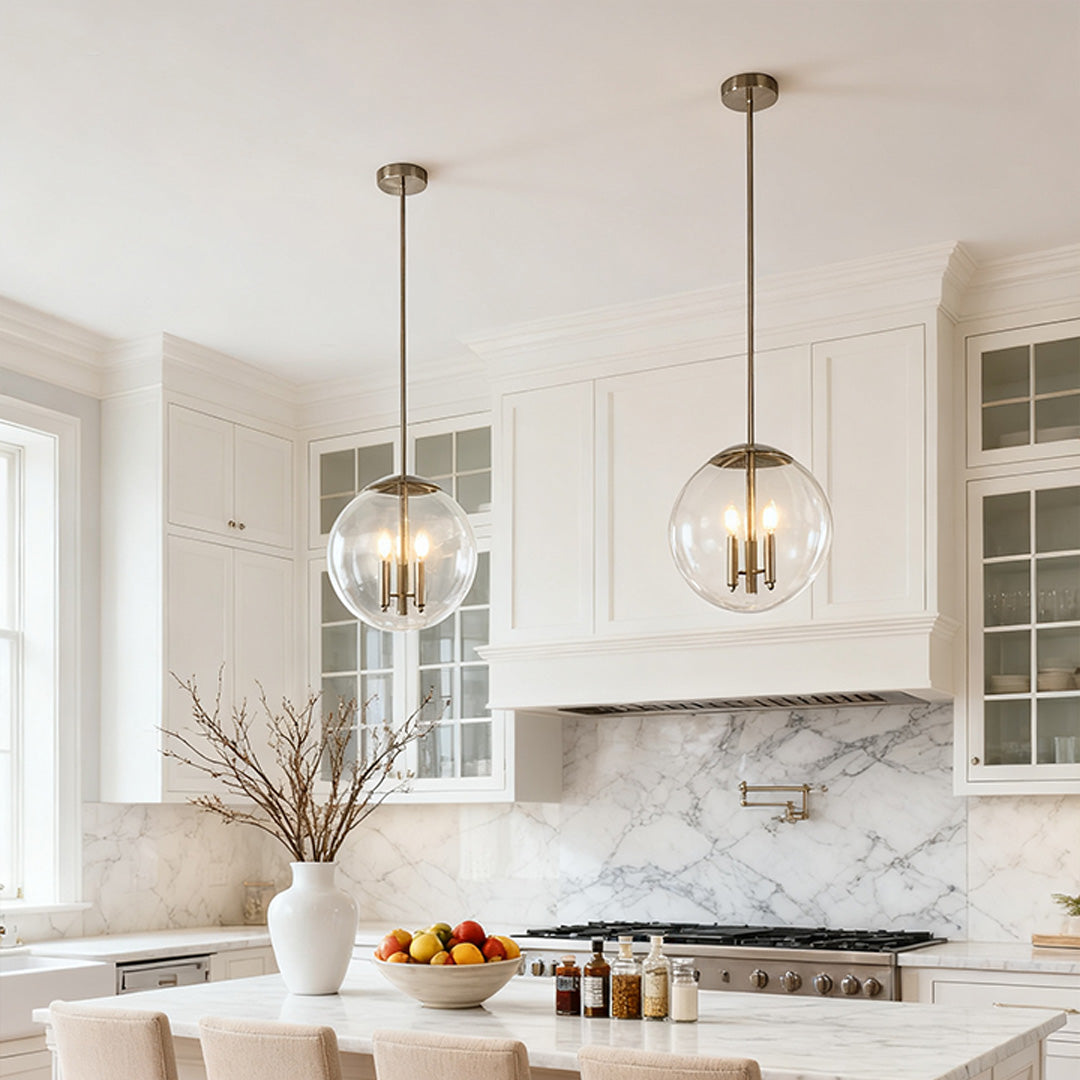 Two clear glass orb pendant light fixtures hanging over a sleek white kitchen island with detailed marble countertops.
