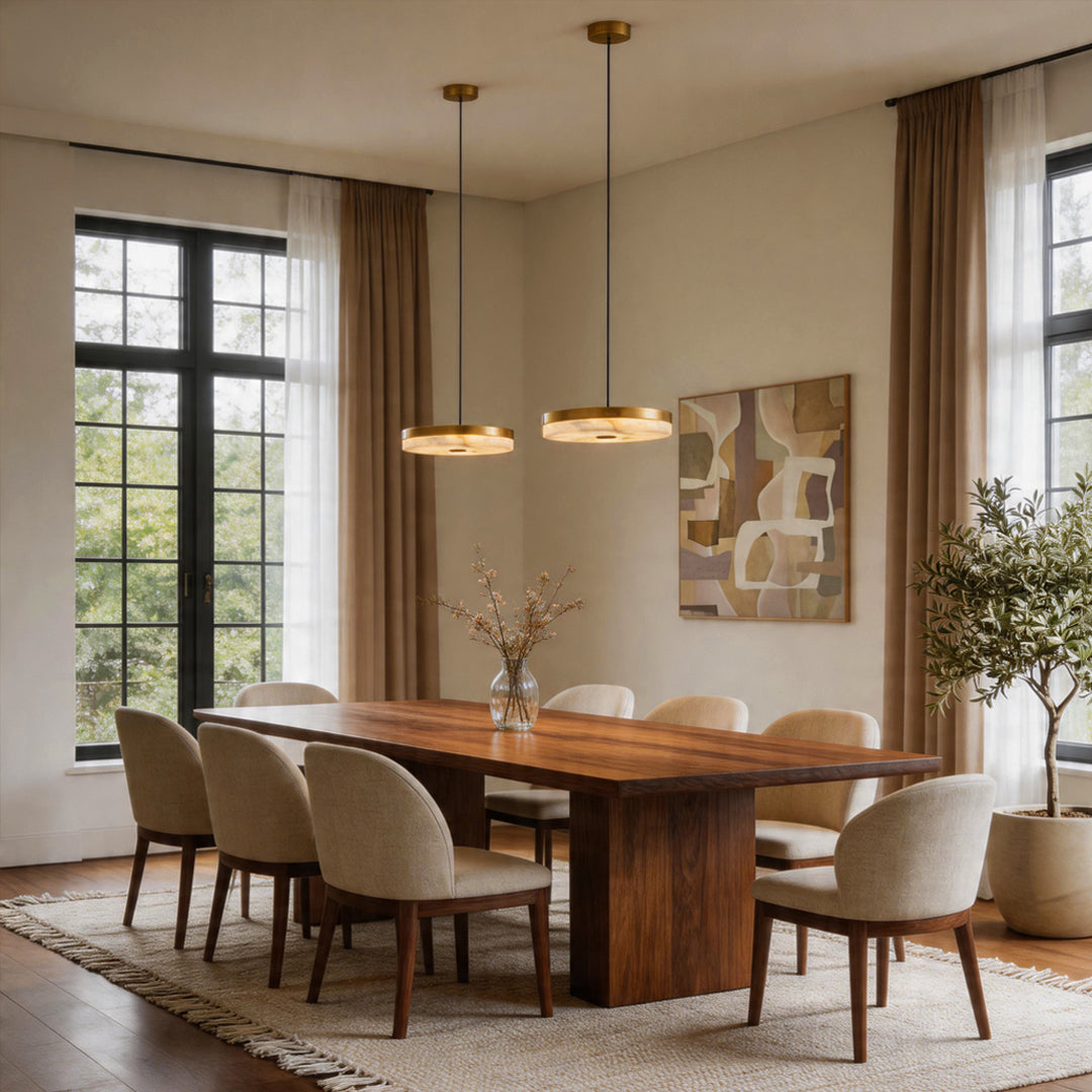 Two disc pendant light fixtures hanging over a large wooden dining table with beige chairs ok.
