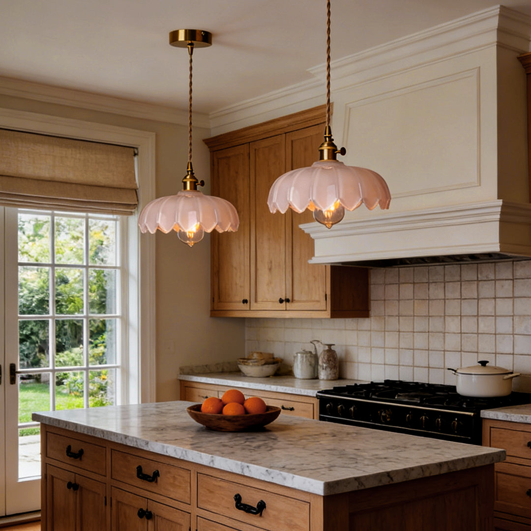 Two glass pendant light with soft pink scalloped shade and brass fixture, glowing warmly in a minimalist indoor setting.