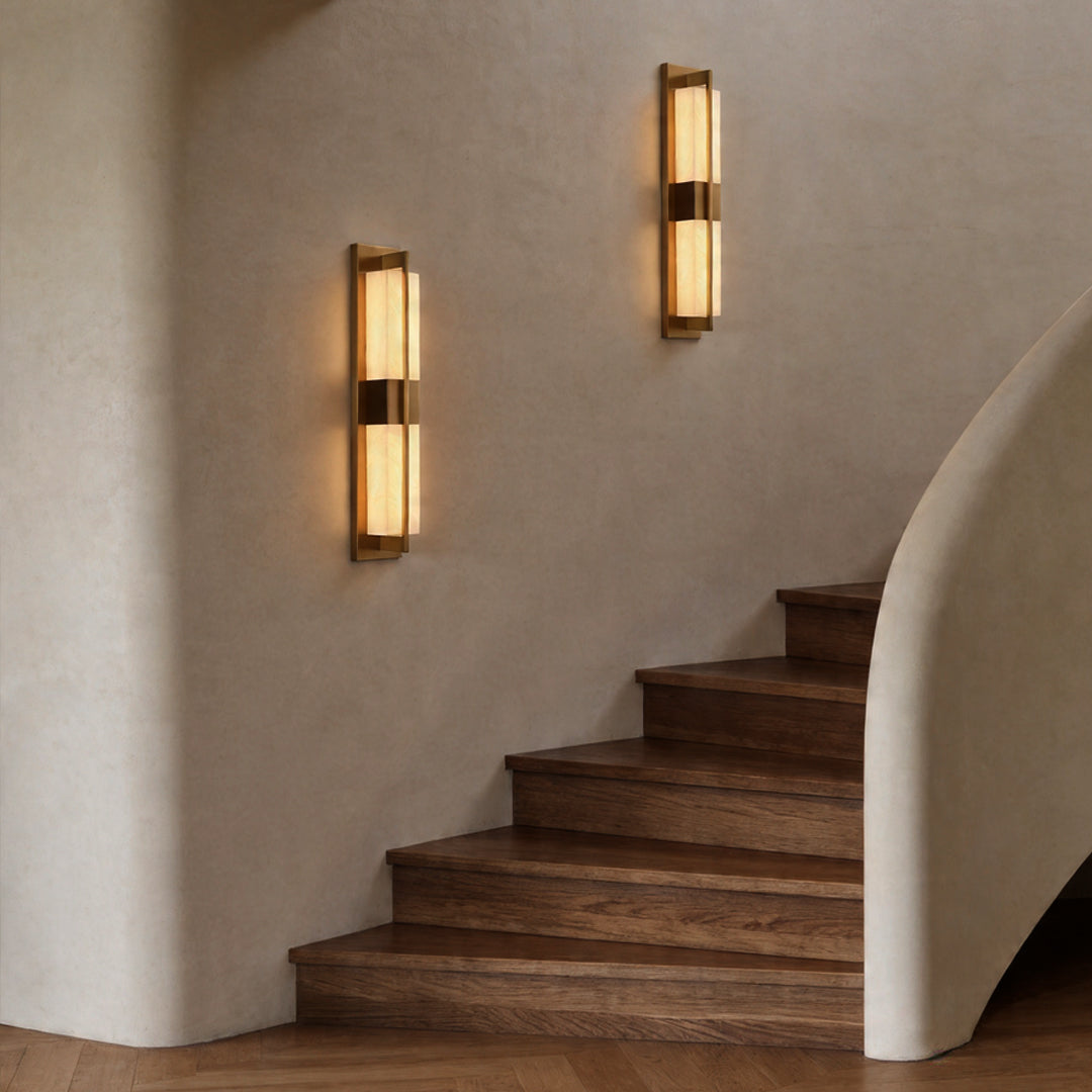 Two gold wall lighting fixtures illuminating a minimalist wood staircase in a modern home ok