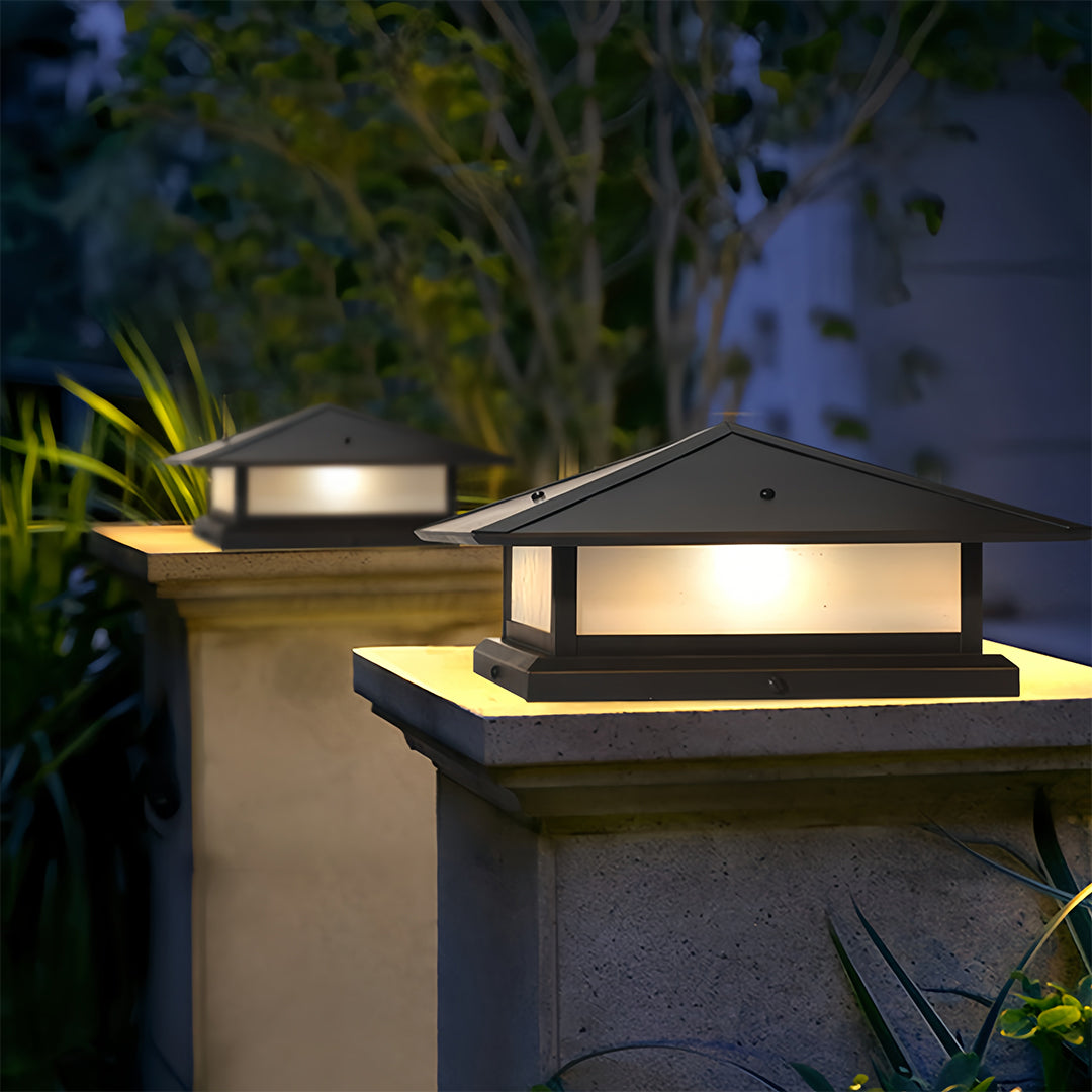 Two modern black pillar lights with tiered, angled roofs mounted on textured sandstone pillars in a suburban garden setting.