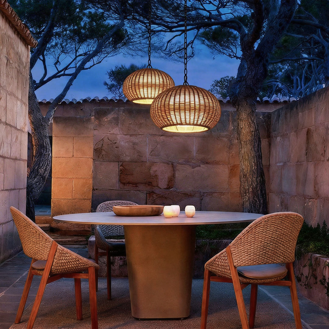 Two rattan outdoor pendant lights hanging above an elegant stone patio dining table at night.