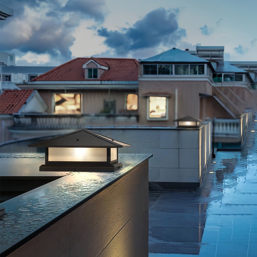 Two black pillar lights installed on a rooftop terrace wall, providing accent lighting on a wet evening.