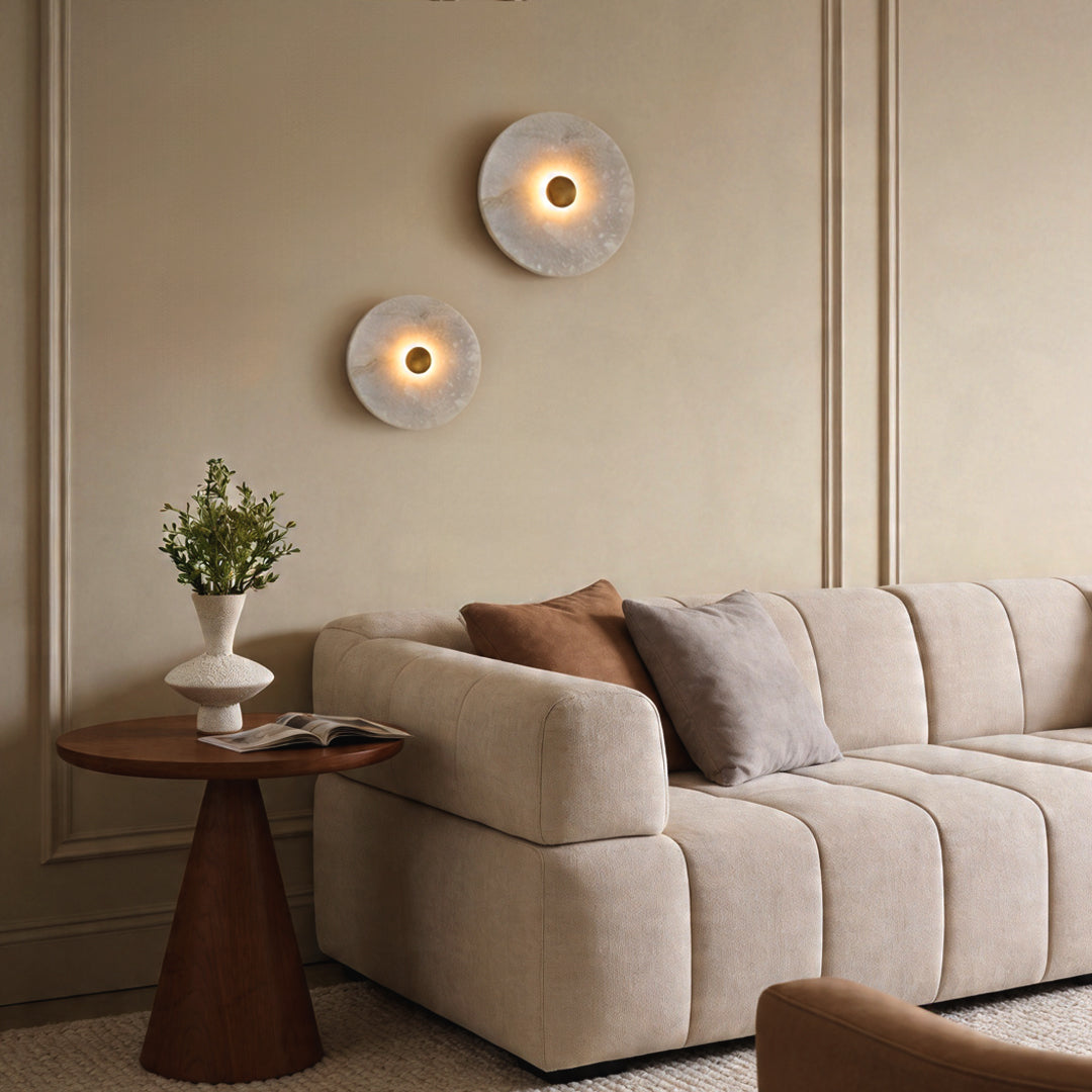 Two round wall lights glowing on a beige paneled wall above a modern sofa in a luxury lounge.