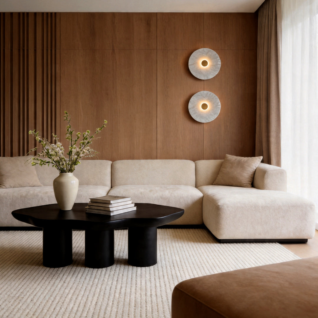 Two round wall lights mounted on a wooden wall above a white sectional sofa in a modern lounge.