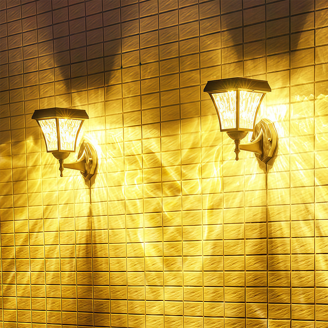 Two solar outdoor sconce lights casting a wide, warm, patterned glow on a tiled exterior wall at night.