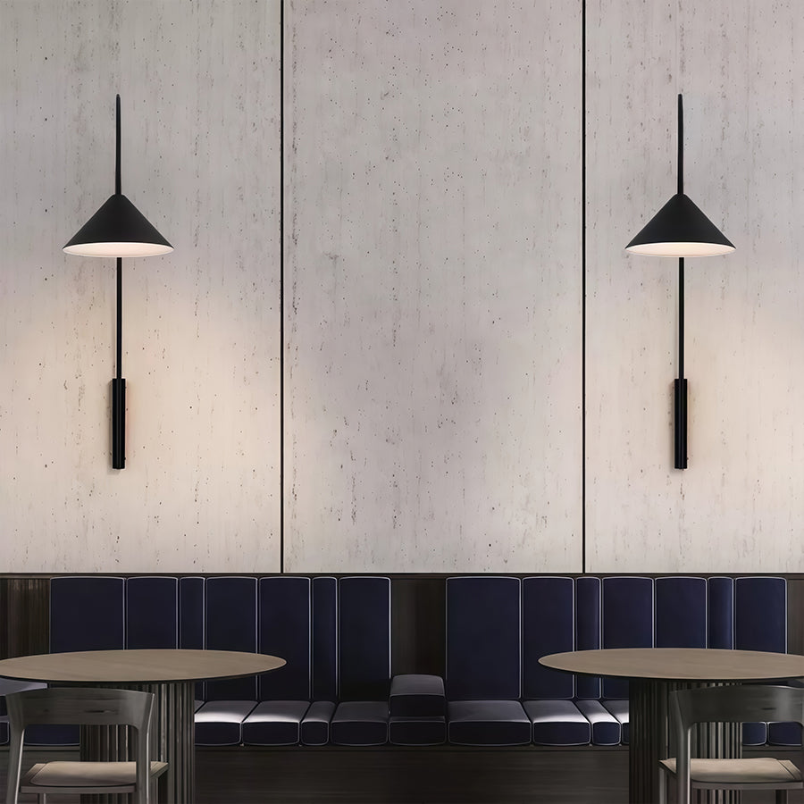 Two wall arm lights with black conical shades hung on grey concrete wall in contemporary restaurant.