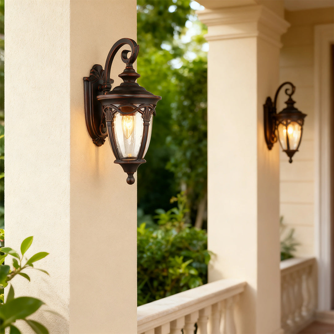 Unique outdoor sconce brightening cream-colored wall near white railing with green foliage backdrop