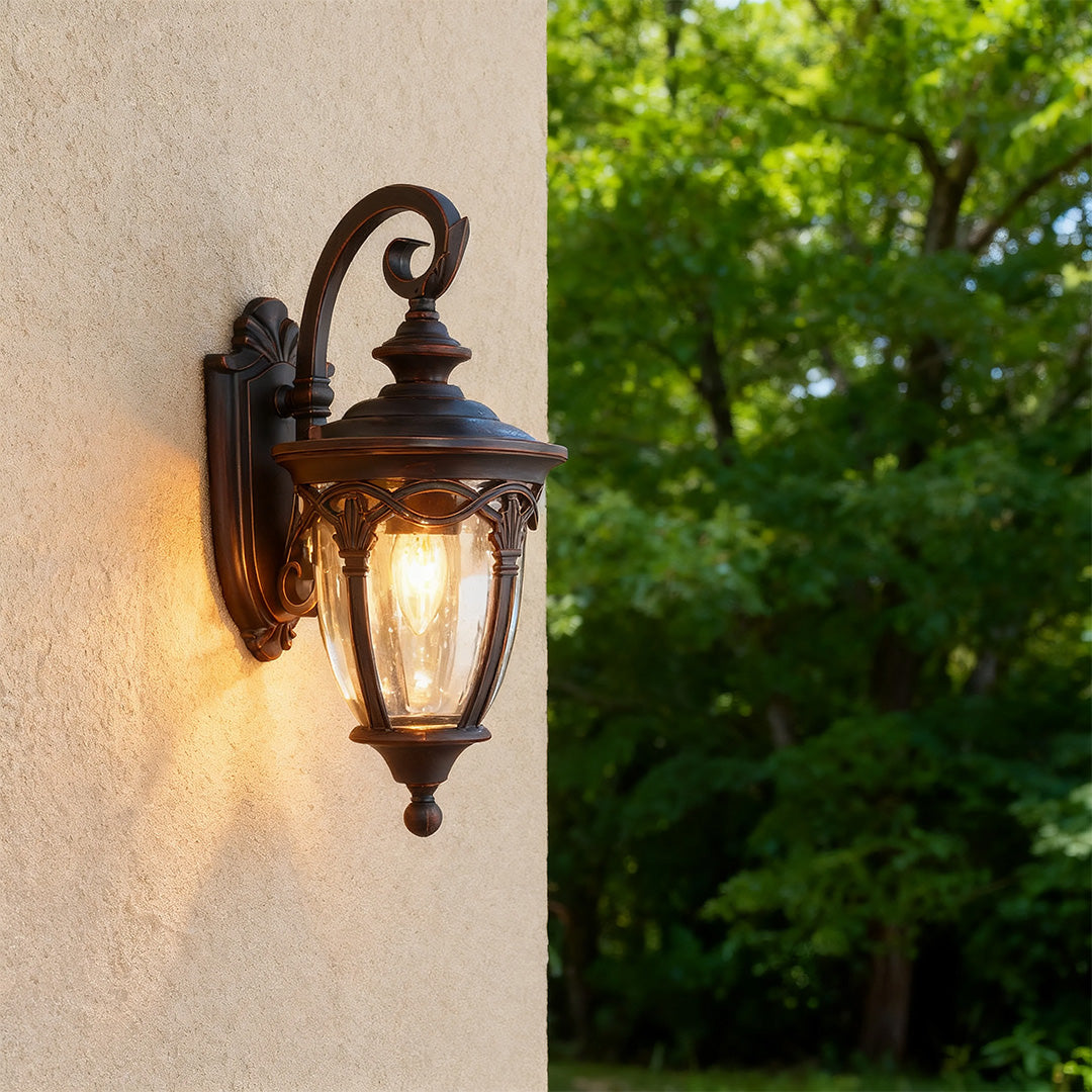 Unique outdoor sconce casting warm golden glow on textured beige stucco wall near greenery