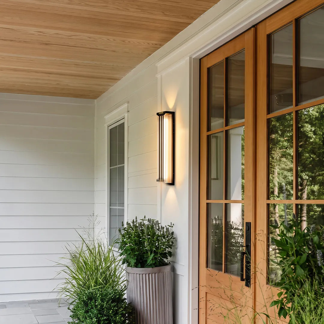 Up and down light wall sconce installed beside wooden framed glass doors on a white exterior wall.