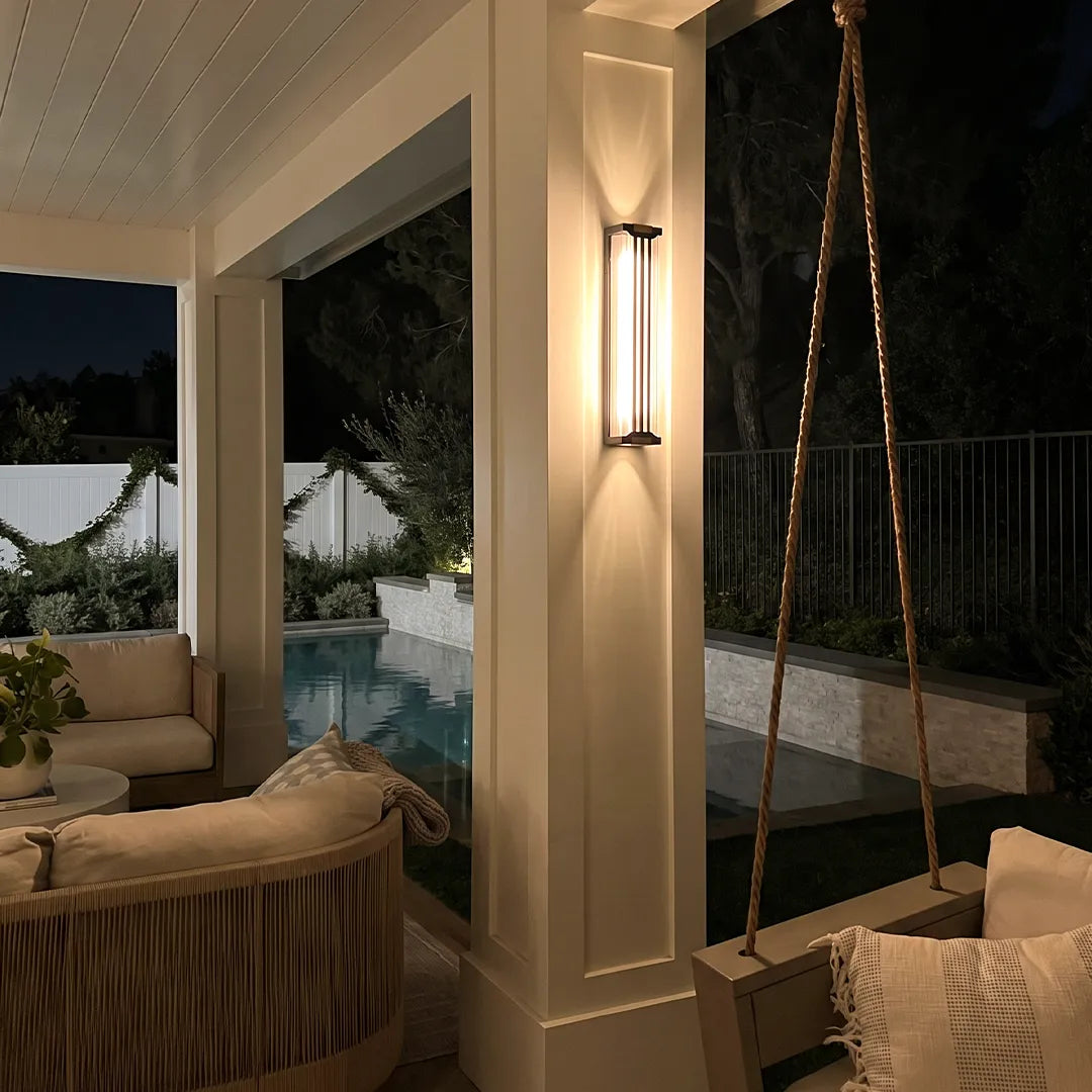 Up and down light wall sconce mounted on a porch column beside a cozy outdoor seating area at night.