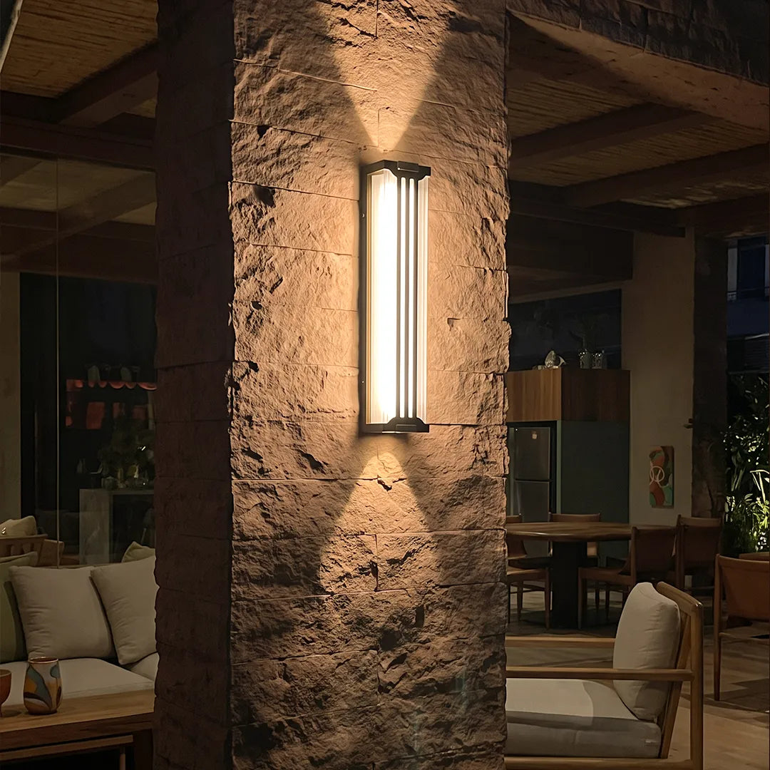 Up and down light wall sconce mounted on a rustic textured column, creating a warm vertical glow in an outdoor dining space.