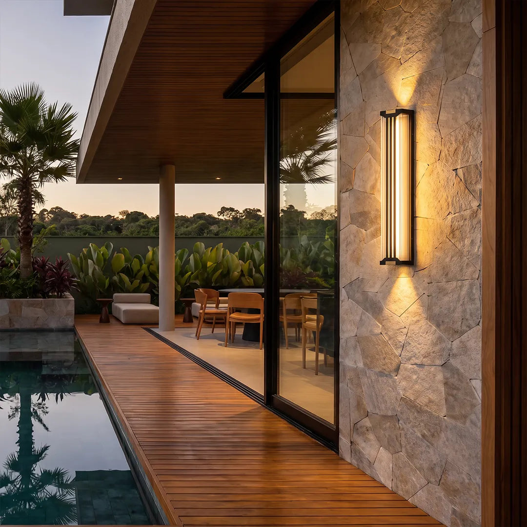 Up and down light wall sconce mounted on a stone exterior wall beside a modern poolside walkway.