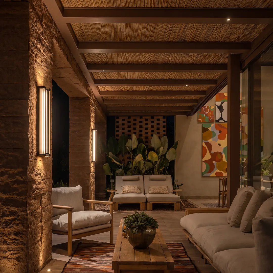 Up and down light wall sconce mounted on a textured patio column, casting warm vertical light in a covered outdoor lounge.