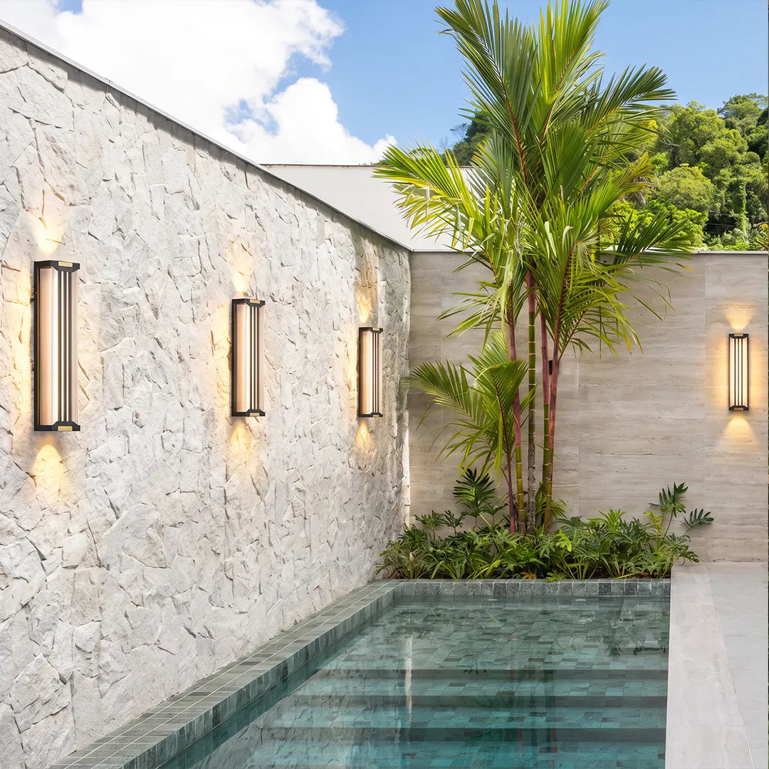 Up and down light wall sconces arranged along a white stone wall beside a swimming pool.
