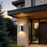 Up down cylinder sconce mounted on a modern home exterior, creating warm vertical light beams that accent stone and wood architecture.