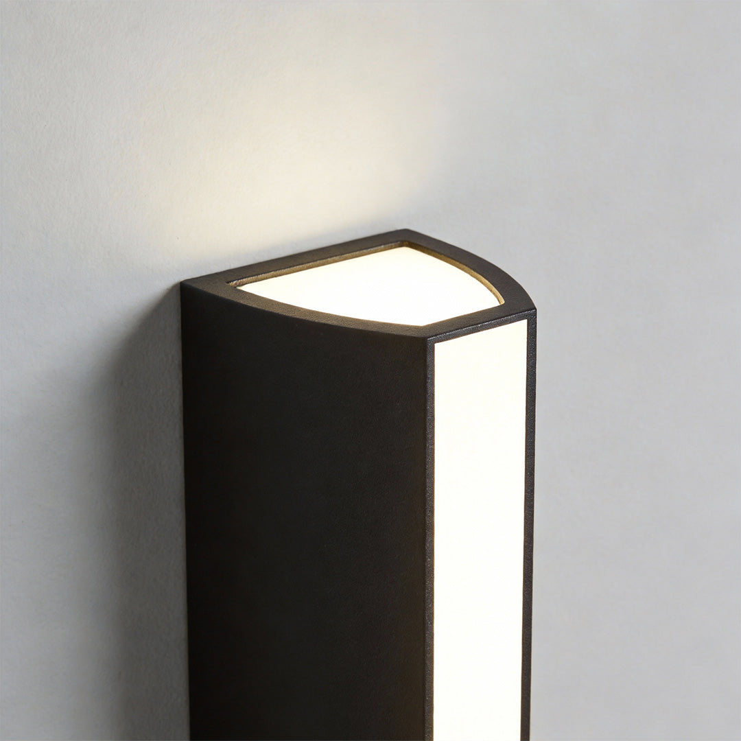 Close-up of an up down cylinder sconce showing the upper light opening and sleek black metal housing.