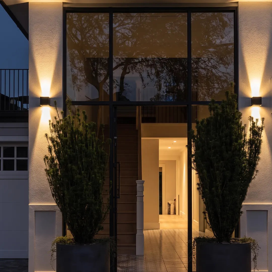 Up down lighting wall lights installed on a modern exterior entry wall with tall windows and warm ambient illumination.