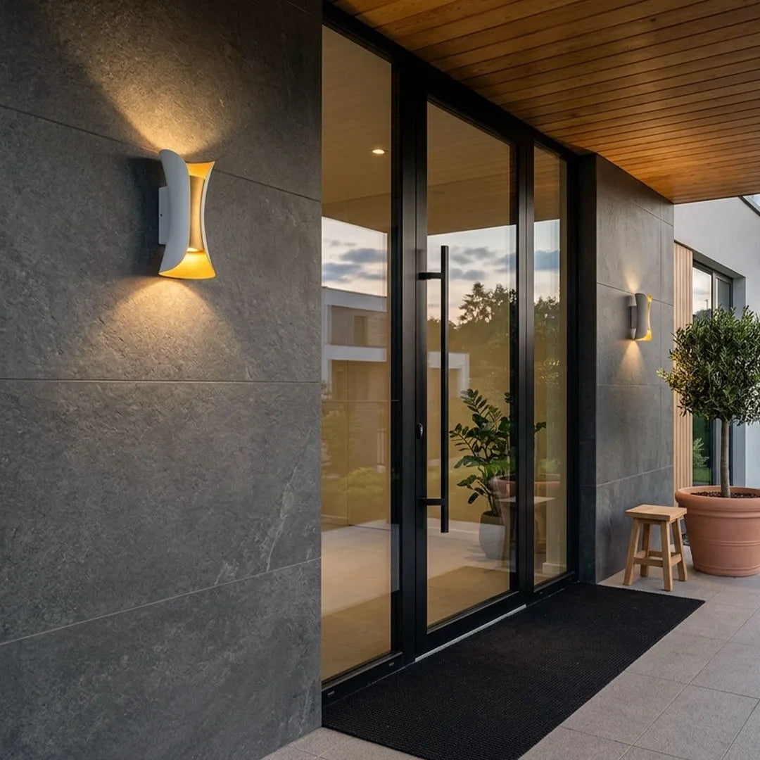Up down lighting wall lights mounted beside a modern glass entryway, casting warm light on a gray exterior wall.