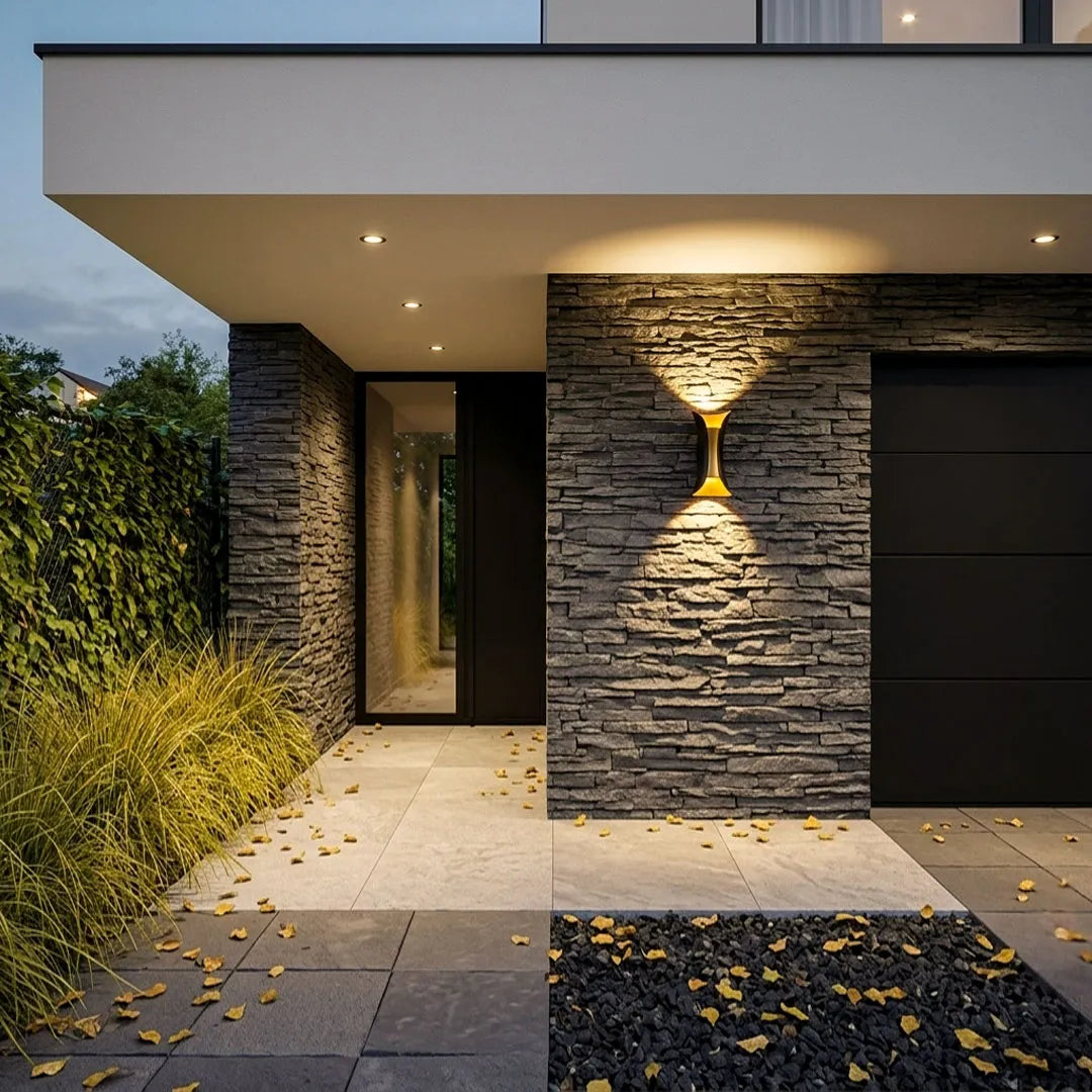 Up down lighting wall lights installed on a dark stone exterior wall, illuminating a contemporary front entrance with warm ambient light.
