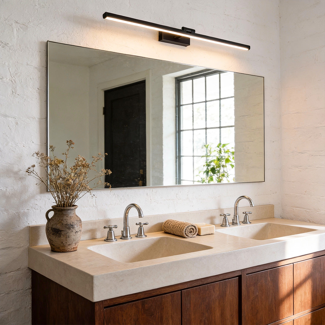 Minimalist bathroom sink area with warm vanity LED lights for mirror mounted above a wide mirror, enhancing natural textures and clean lines.
