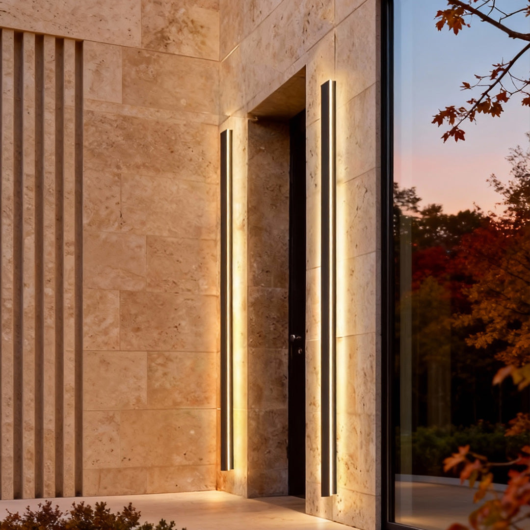 Sleek vertical linear outdoor wall sconce installed on beige stone facade, providing modern and warm illumination.