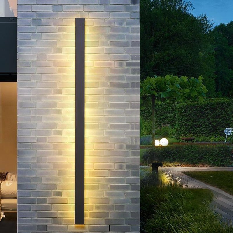 Vertical linear outdoor wall sconce with soft glow, enhancing the entrance of a modern house with wooden accents.