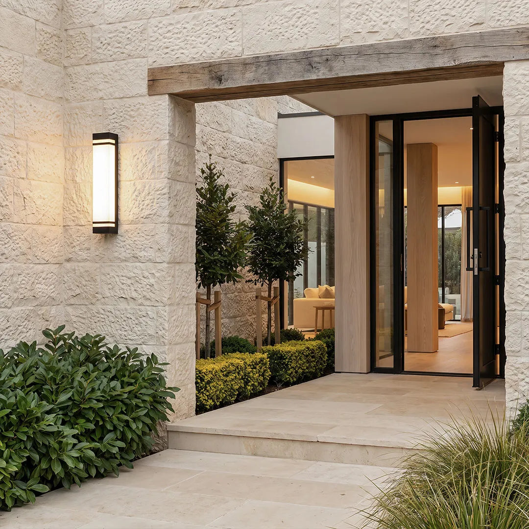 Vertical wall lighting mounted beside a contemporary front entrance with textured stone walls and landscaped greenery.