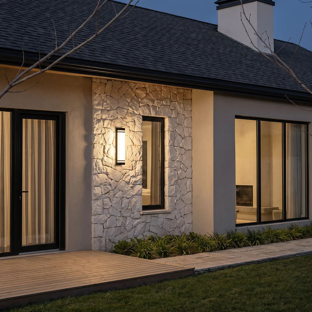 Vertical wall lighting installed on a modern stone exterior wall, adding warm architectural illumination beside tall windows.