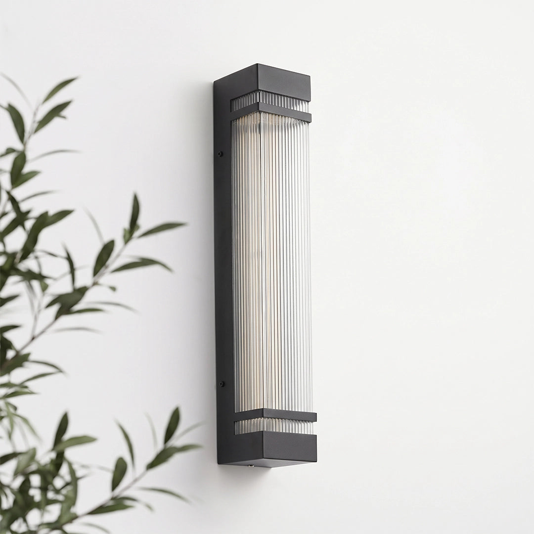 Vertical wall lighting with a slim black frame and clear ribbed shade mounted on a white wall.