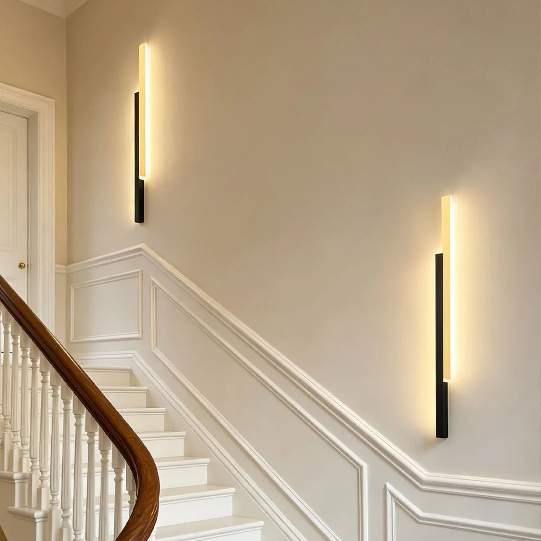Vertical wall lights installed along a curved staircase wall in an elegant interior hallway.