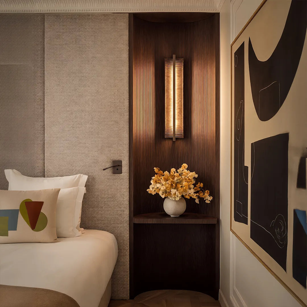 Vertical wall sconce with warm glow beside bed and decorative wood panel