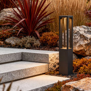 LED bollard garden light with vertical light strips, positioned beside colorful plants for stylish outdoor lighting