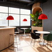 Three vibrant red colored pendant light fixtures hanging over a bar and seating area in a modern cafe space.