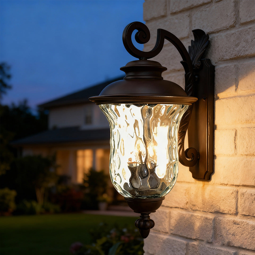Vintage black exterior wall light glowing warmly on tan brick wall at dusk with house backdrop
