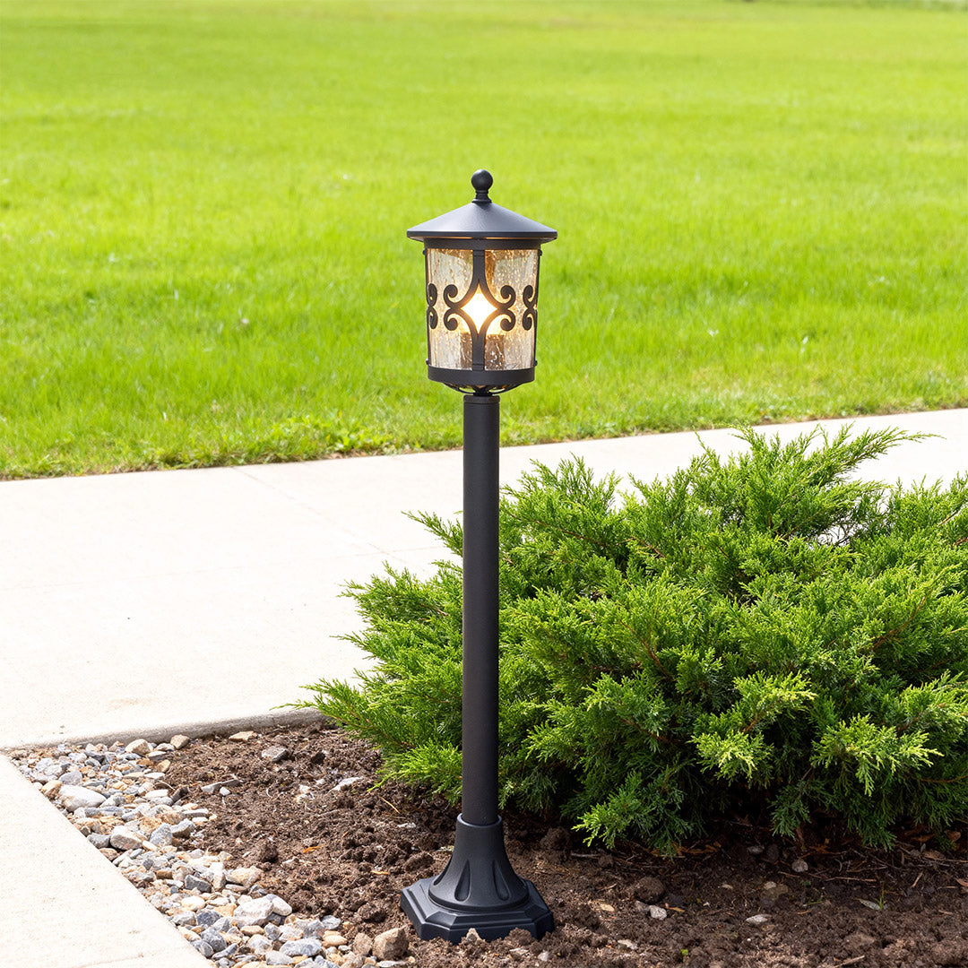 Vintage style bollard LED light brightening concrete pathway edge with manicured lawn and shrubs