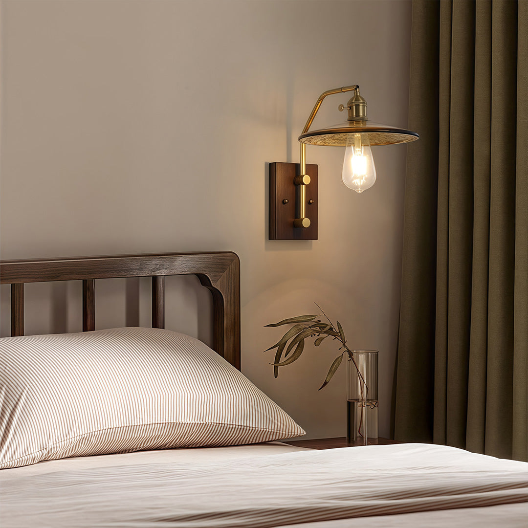 Vintage brass and glass wall lights with a disc shade, mounted above a wooden bed frame in a cozy bedroom setting.