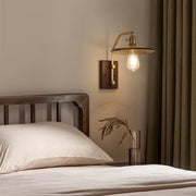 Vintage brass and glass wall lights with a disc shade, mounted above a wooden bed frame in a cozy bedroom setting.