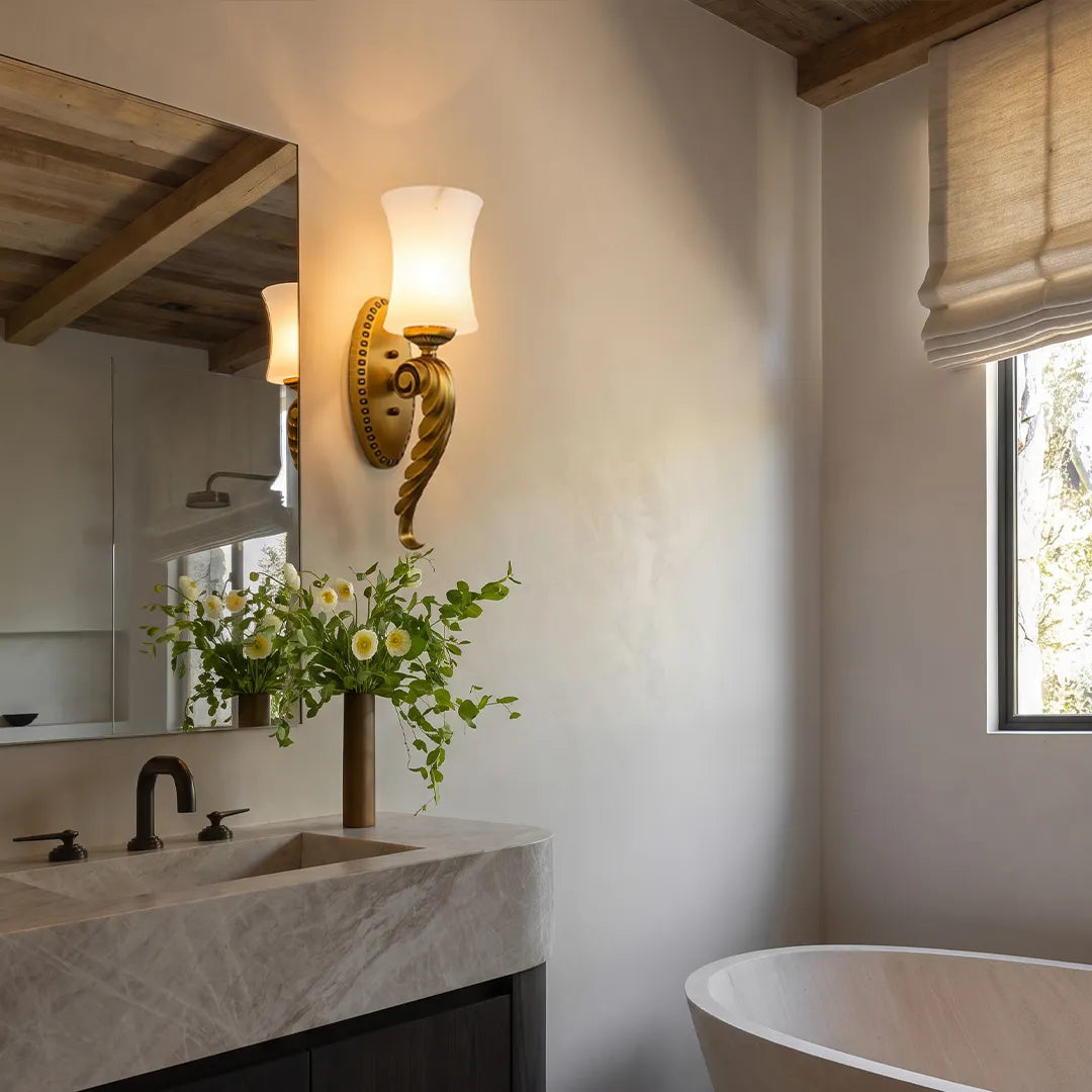 Vintage brass wall sconce above a bathroom vanity with a sculpted brass base and frosted glass shade.
