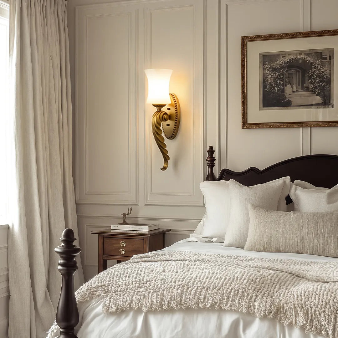 Vintage brass wall sconce mounted beside a bed with a frosted glass shade and warm ambient glow.